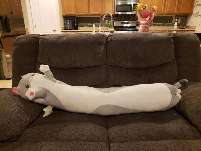 reviewer photo of a 53-inch cat-shaped plushie lying horizontally on a couch