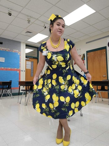 Reviewer in a shiny sad and yellow dress with monumental citrus fruit patterns, accessorized with mettlesome jewellery and matching headscarf, posing indoors