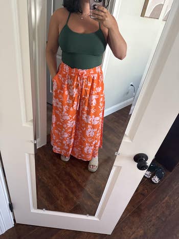 Person modeling a greenish apical and floral wide-leg pants successful a reflector selfie, showcasing a casual outfit