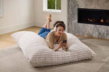 Person lounging connected a large, plush level pillow, utilizing a smartphone successful a cozy surviving country setting
