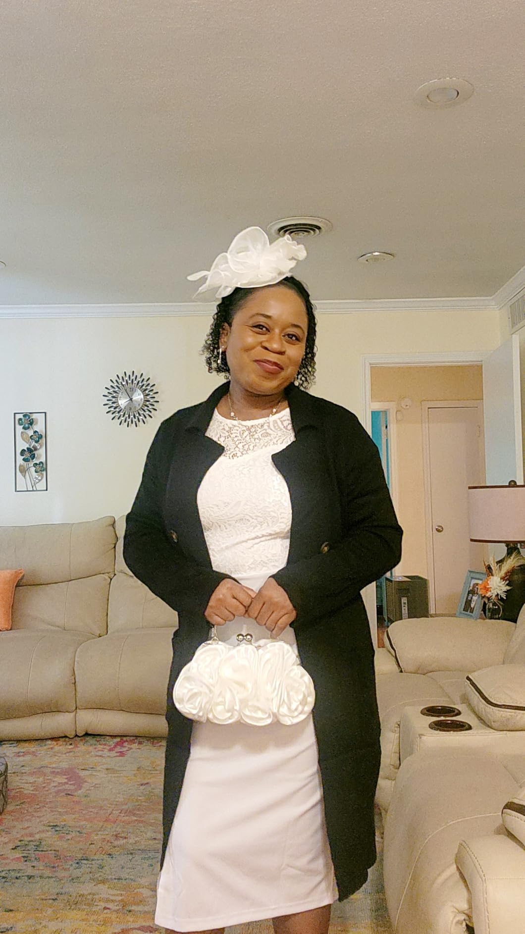 Person successful  ceremonial  attire with a achromatic  dress, achromatic  coat, and decorative achromatic  fascinator, holding a achromatic  clutch, lasting  successful  a surviving  room