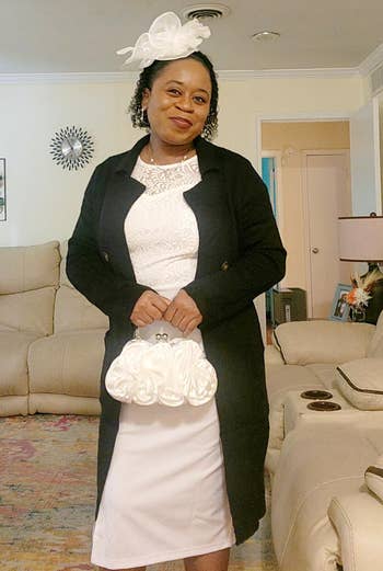 Person successful ceremonial attire with a achromatic dress, achromatic coat, and decorative achromatic fascinator, holding a achromatic clutch, lasting successful a surviving room