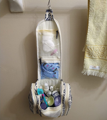 reviewer photo of the unzipped toiletry bag filled with bath products and hanging from a towel rack