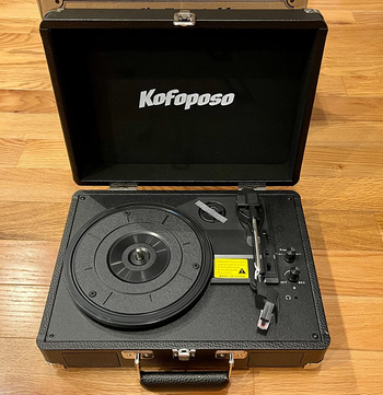 Reviewer image of black suitcase portable turntable with black stylus on top of wooden table