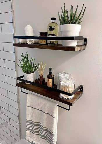 reviewer's brown shelves above the toilet holding plants and various toiletries