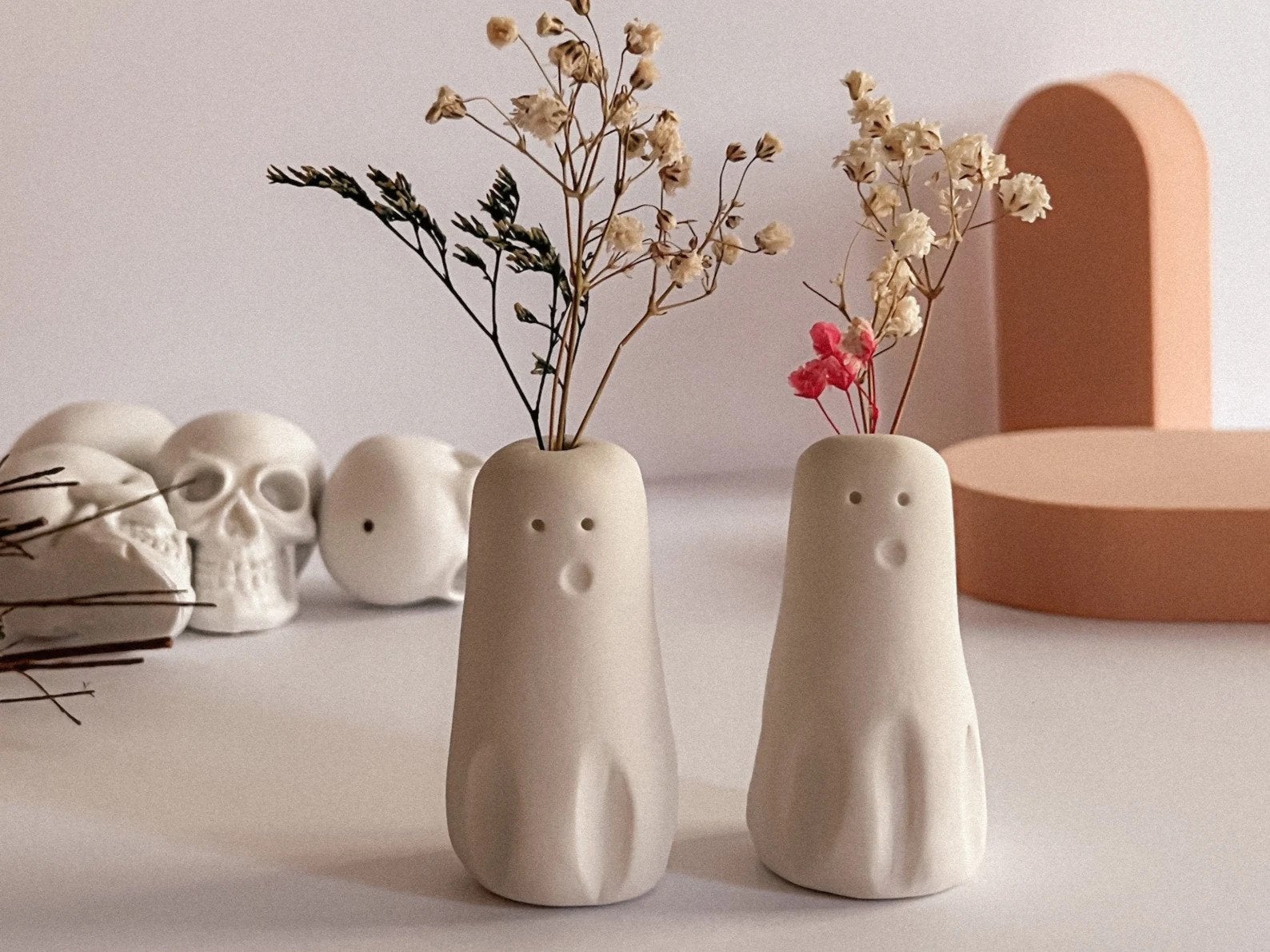 two tiny carved minimalist ghost vases with small stems of flowers coming out of the top