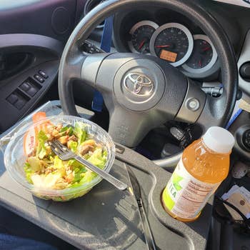 Salad and iced tea on a car steering wheel, suggesting convenience for eating on-the-go