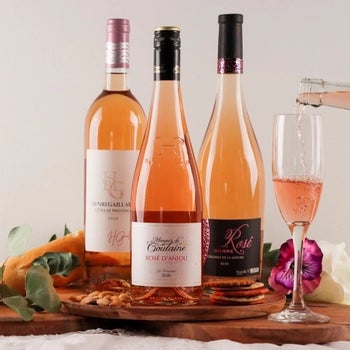 three bottles of rose next to a glass being filled with rose