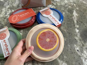 Hand holding a silicone nutrient  screen  with a grapefruit print, shown with different   colour  variations. Packaging reads 