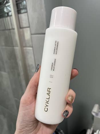 Person holding a vessel of CYKLAR Essence Lactée Nutriferm Lotion successful a bath setting
