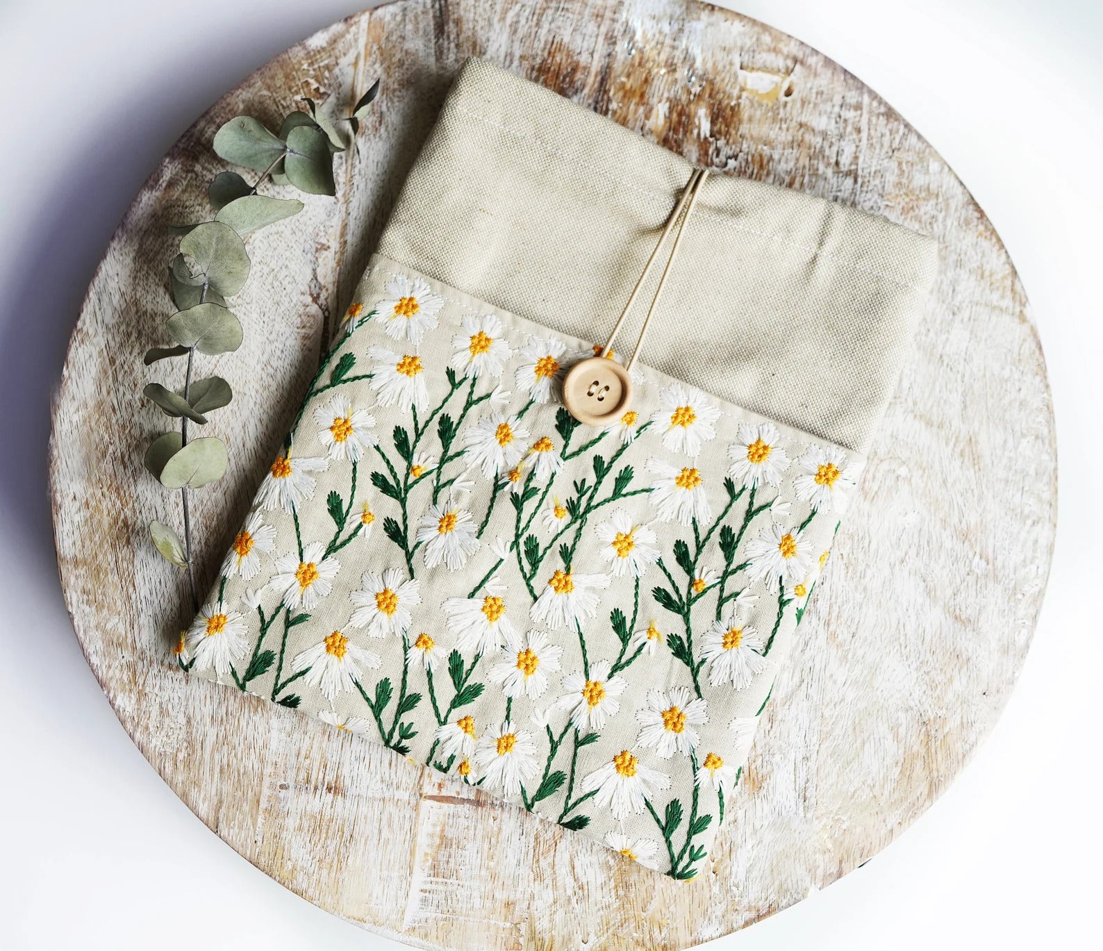 the cream colored daisy embroidered book sleeve with a button tie closure 