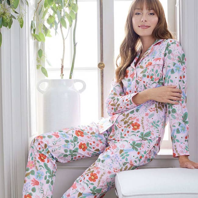 model wearing pink pajama set with floral and strawberry plant pattern on it