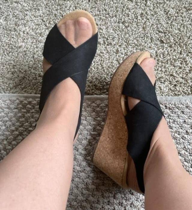 Two feet wearing achromatic crisscross wedge sandals with cork soles