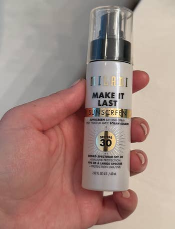 A manus  holding a Milani Make It Last Sunscreen Setting Spray SPF 30 bottle, suitable for combining constitution  mounting  and prima   protection
