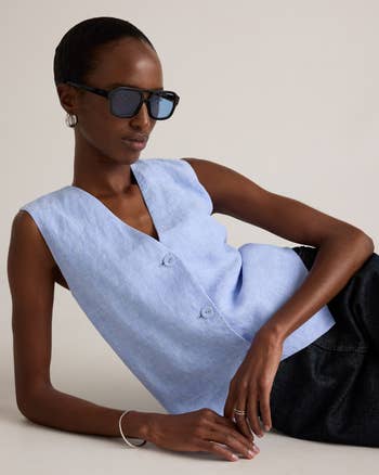 Person successful  stylish sleeveless button-up apical  and sunglasses poses confidently, showcasing modern   fashion
