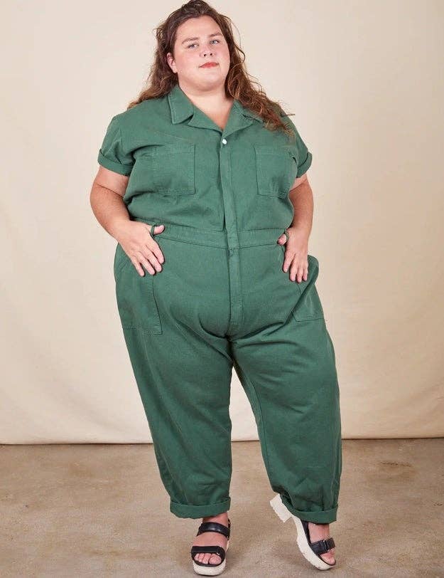 Model in green jumpsuit with hands on hips, posing in a studio 