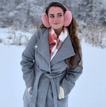 reviewer wearing the pink earmuffs with a gray coat in the snow