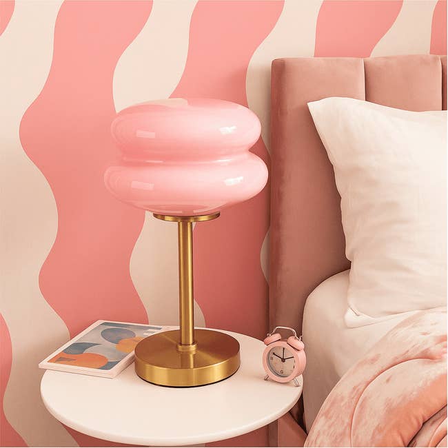 Modern chamber with a pinkish lamp, matching clock, and abstract-patterned wall. Cozy decor items suggest existent buying trends