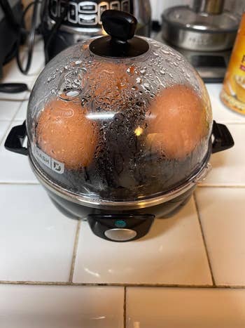 Egg cooker connected  a room  antagonistic  with 2  eggs inside, steam covering the lid