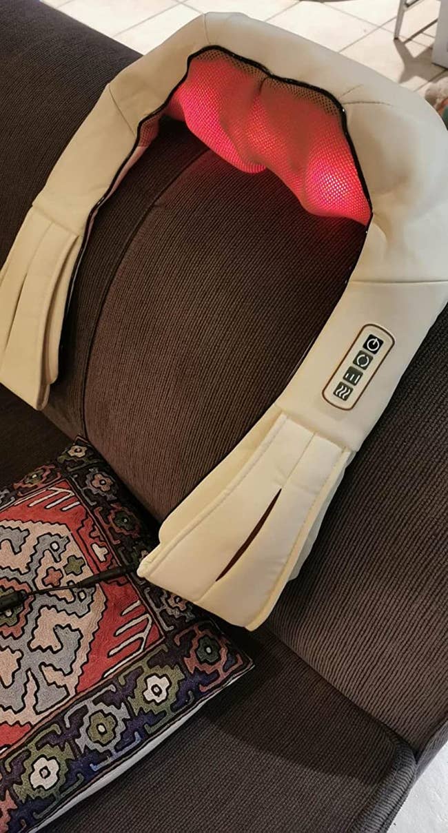 reviewer photo of white shoulder massager glowing with heat, on the back of a couch