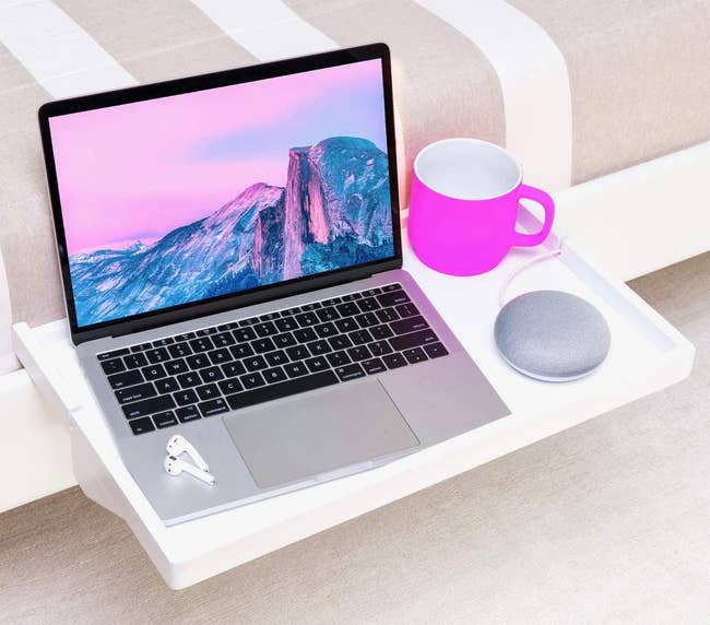a white shelf mounted onto a bed frame with a mug, speaker, and laptop sitting on it 