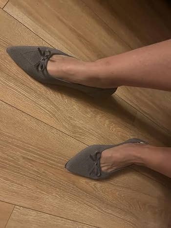 Person wearing pointed, textured flats with bow detail, lasting  connected  a woody  floor