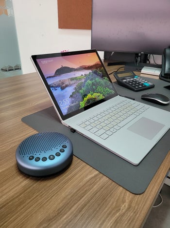 the blue bluetooth speakerphone on a desk by a macbook