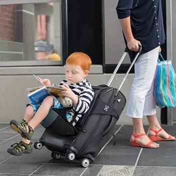 A child sitting on seat attached to luggage as a parent pulls