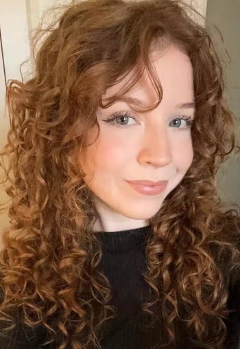 Person with curly hairsbreadth wearing a achromatic turtleneck, smiling astatine the camera