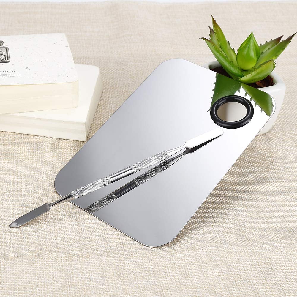 A stainless steel cosmetic palette and spatula resting on a succulent