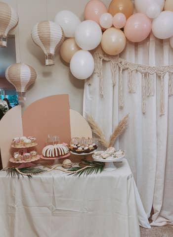 reviewer's cake corner at a party with three air balloon lanterns propped up in a corner beside a balloon garland