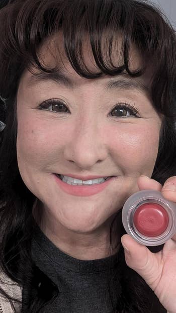 Person smiling and holding a tiny  instrumentality  of reddish  articulator  balm, suggesting quality   and buying  theme