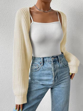 Person in a white tank top and cream colored cropped knit open cardigan