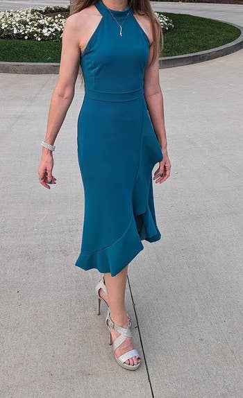 Person in a halter-neck, teal dress with an asymmetrical hemline, paired with white strappy heels