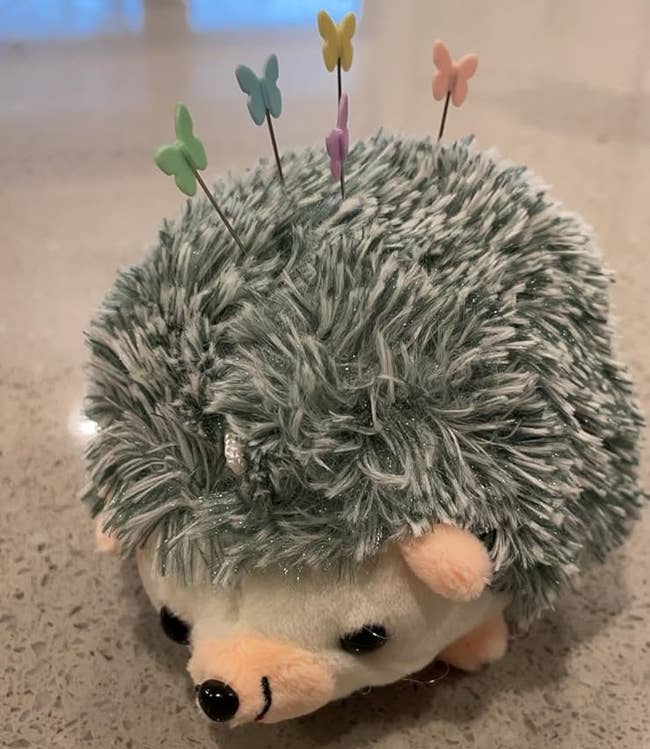 Plush hedgehog pin cushion with butterfly-shaped pins on its back