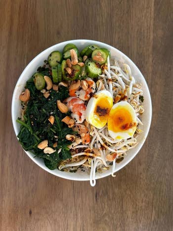 Reviewer's bowl of ramen with egg, greens, sprouts, nuts, and cucumber
