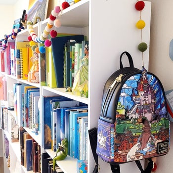 a reviewer's beauty and the beast loungefly backpack hanging off of their shelf