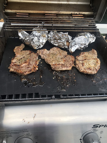 reviewer photo of steaks cooking on the grill mat