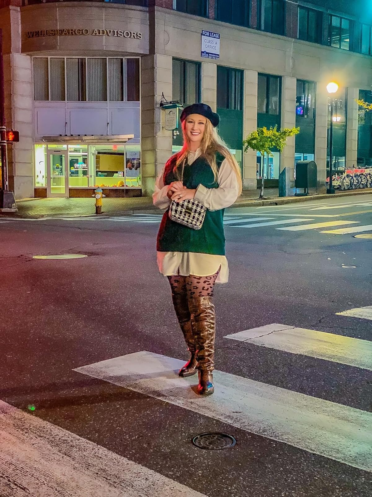 Person stands connected  a metropolis  thoroughfare  wearing a beret, agelong  shirt, greenish  sweater vest, leopard people     tights, and knee-high boots, holding a patterned clutch