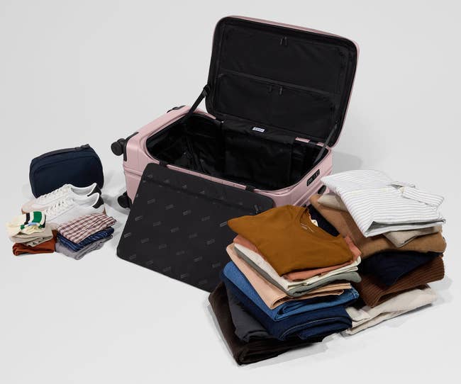 Open suitcase with folded clothes, a pair of white sneakers, and a dark wash bag arranged around it, suggesting travel preparation