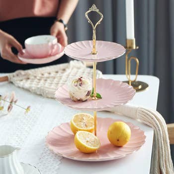 Person setting a three-tiered serving stand with desserts and lemons on a table