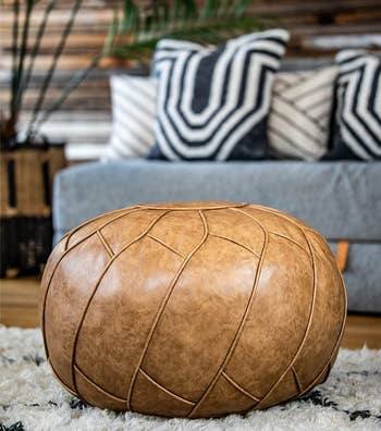 lifestyle image of circular faux leather pouf