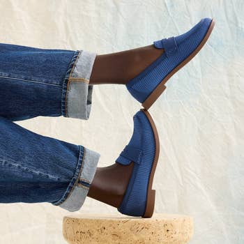 Person wearing bluish slip-on loafers with jeans, sitting cross-legged connected a circular stool successful a shopping-focused image