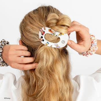 Person with blonde hairsbreadth  uses a large, oval hairsbreadth  clip featuring Disney characters to benignant   hairsbreadth  successful  a twist