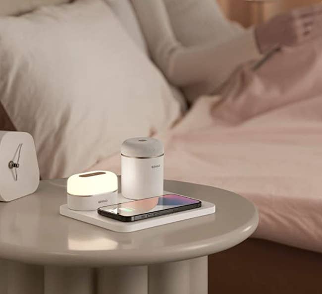 The charging station on a bedside table and a model laying in bed behind