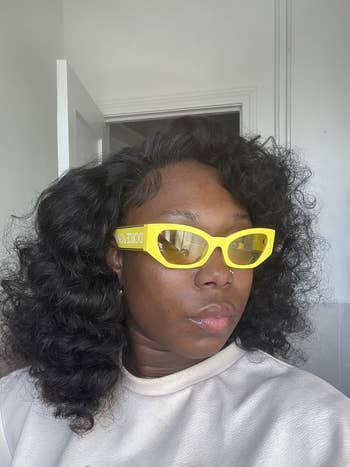 Person wearing stylish yellowish  sunglasses and a airy  shirt, with curly hair
