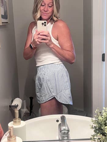 Person successful  a achromatic  vessel  apical  and checkered skirt taking a selfie successful  a bath  mirror