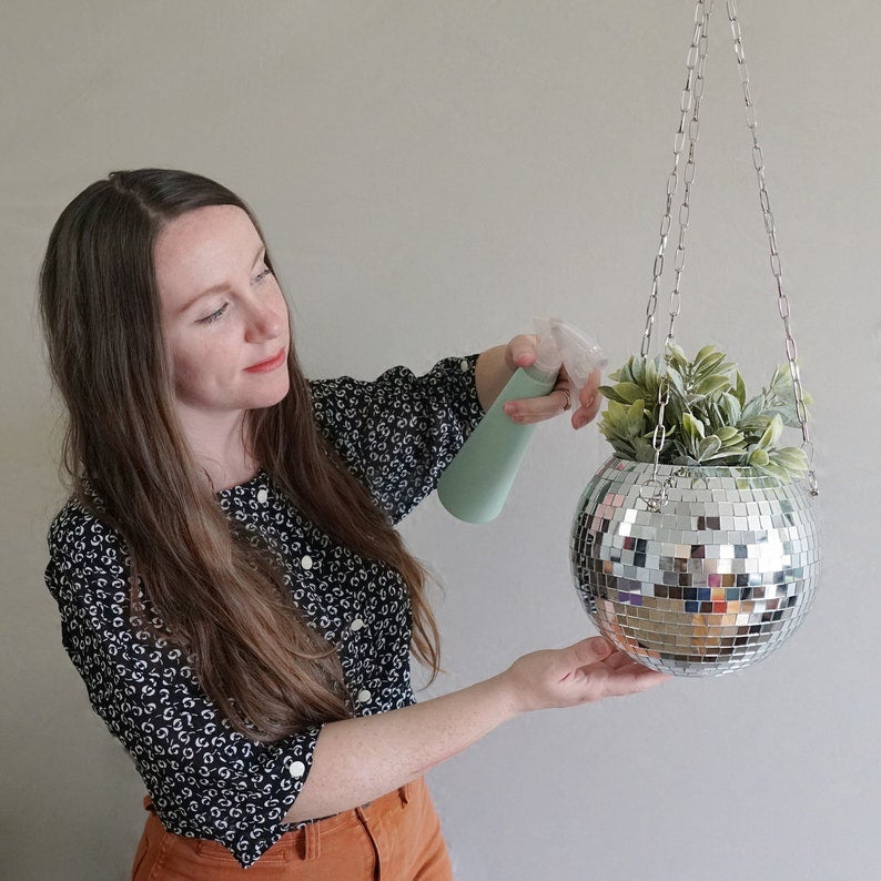 person watering a plant in a hanging disco ball planter