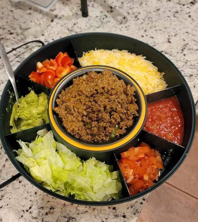 Sectioned round tray with taco ingredients: ground meat, lettuce, cheese, tomatoes, salsa, and peppers
