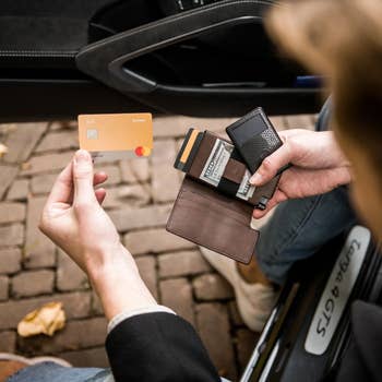 Person sitting in a car seat, holding a bank card and an open wallet with cash and cards, suggesting a shopping or payment context